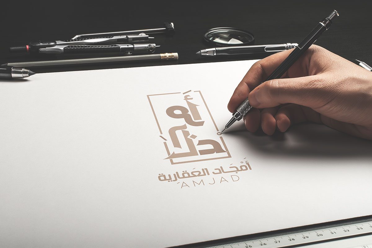 realistic view du logo Amjad real Estatede la création graphique, au Webdesign, au SEO optimisation des moteurs de recherche à la mise en place d'une stratégie de marketing digital une main qui dessine le logo avec un stylo